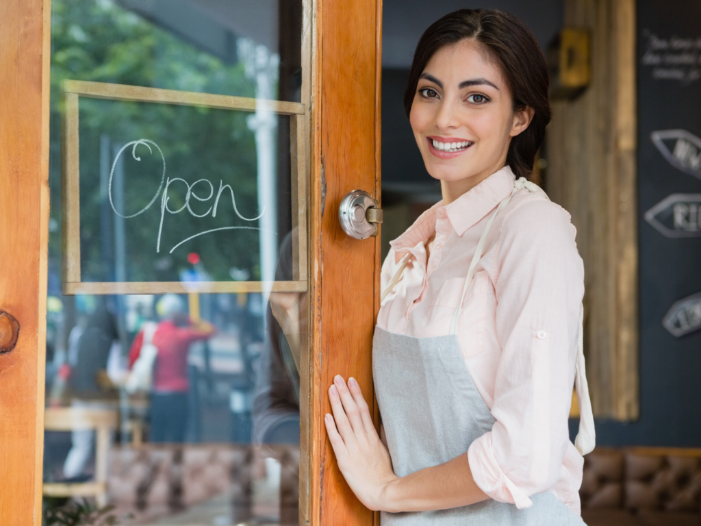 a woman standing in front of her cafe by an open sign that she keeps successful by using a strategy for financial management for restaurants