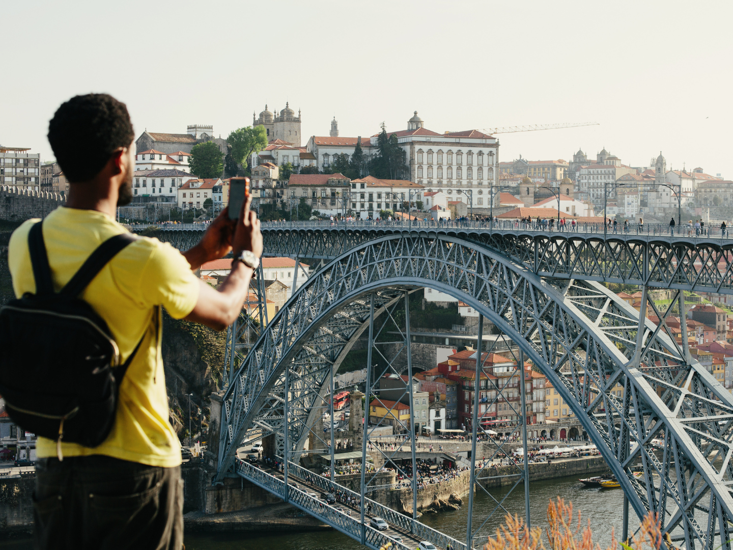 a man in a yellow shirt taking a photo of a bridge in portugal on a trip he took after his CD matures