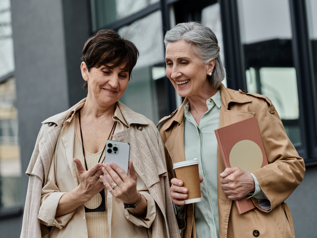 a mature female presenting couple wearing trench coats and fall garments drinking coffee while reviewing options after CD maturity on a phone