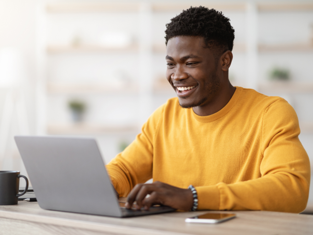 a man with short dark hair and deep brown skin in a yellow sweater sits at his computer studying the benefits of CDs for young professionals