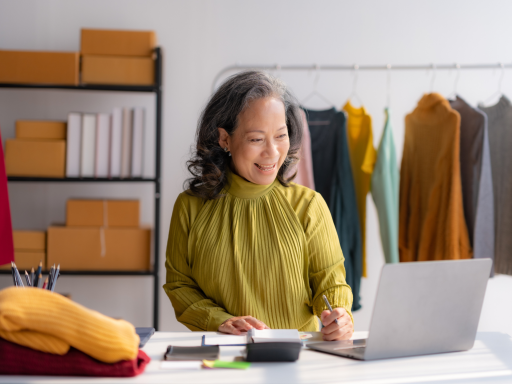 a senior woman with medium tan skin and black and gray hair manages her clothing store from her computer in a space funded with the sba 7(a) loan program