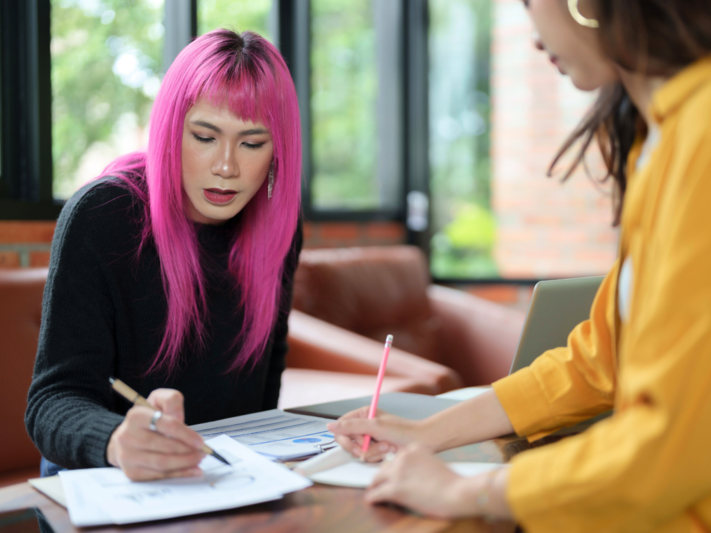 a small business owner with long pink hair and pale skin reviews CD strategies  with their teenage daughter for upcoming educational expenses