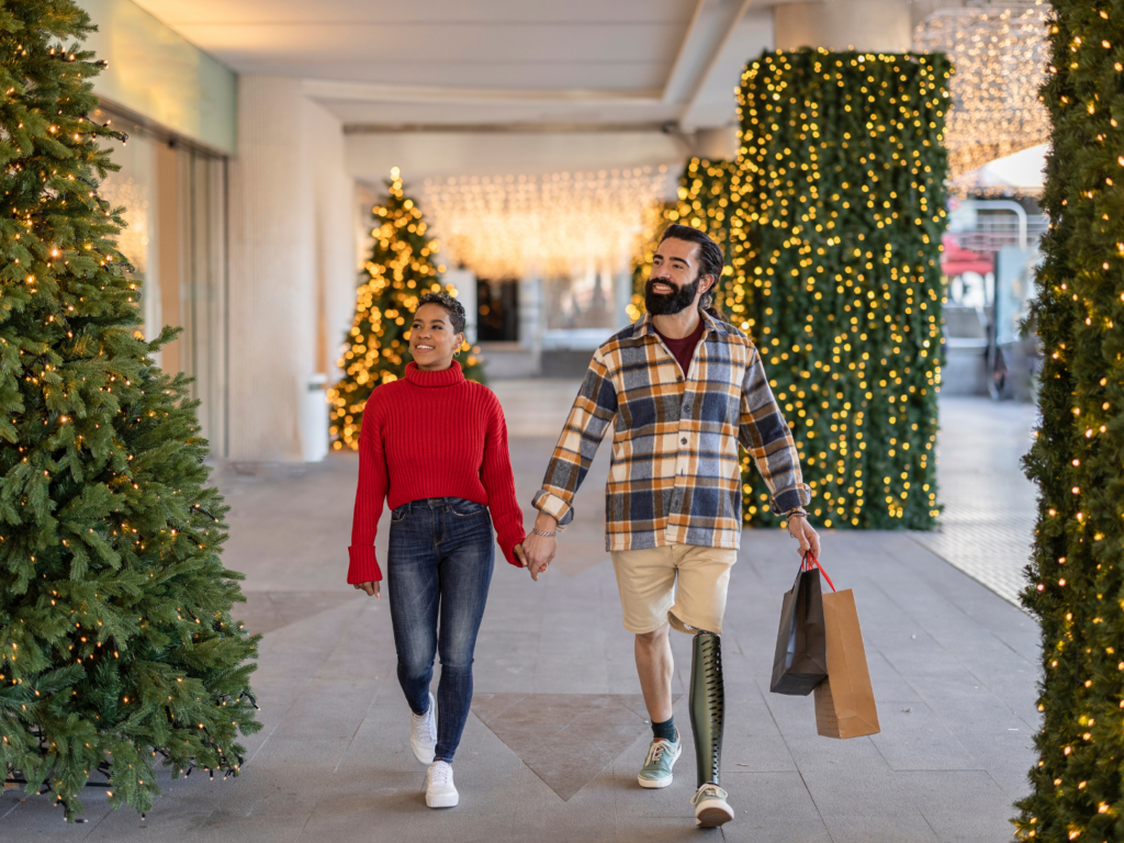 a woman with medium brown skin and short hair and a man with dark hair and a prosthetic leg holiday shopping hand in hand who used the best CDs to save for a big purchase