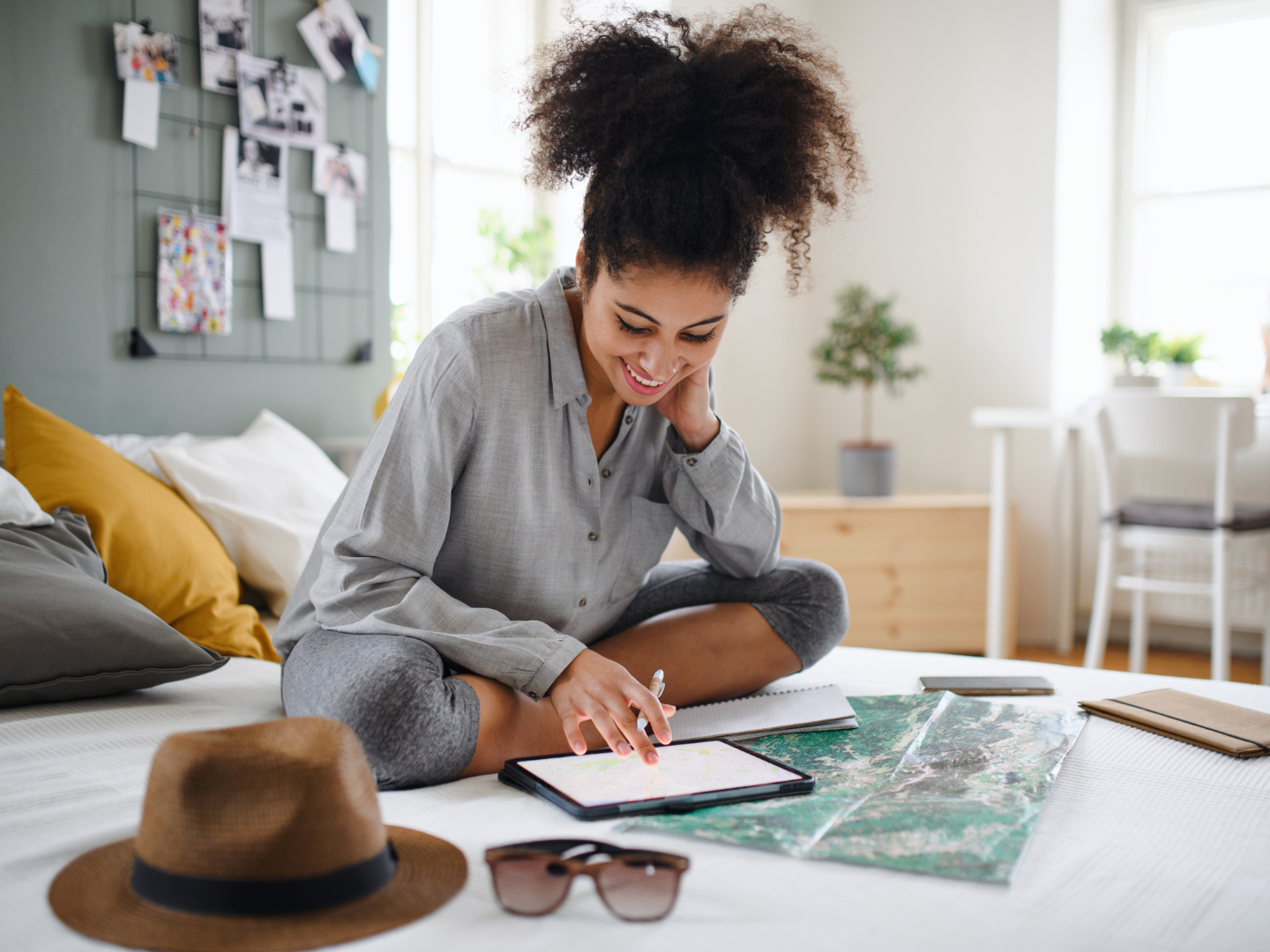 a woman with medium brown skin with dark curly hair sits on her bed planning a dram vacation that she is planning to use a cd for a major purchase